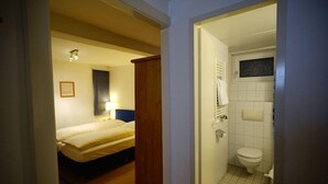 A hotel room with a bed, a bedside lamp, a wooden door, and a bathroom with a toilet and sink. - Md-rabe's Hotel Kiel (Kiel)