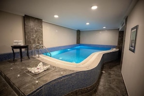 Een rechthoekig bubbelbad met een blauwe betegelde binnenkant, een klein tafeltje met handdoeken en een aan de muur bevestigd fotolijstje.