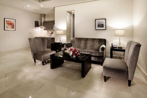 Een zithoek met een bank, twee fauteuils met een patroon, een bijzettafeltje met bloemen, een nachtkastje met een lamp en kunstwerken aan de wanden.