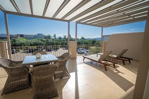 Un espacio exterior cubierto con una mesa, sillas, una tumbona y vistas del paisaje circundante.