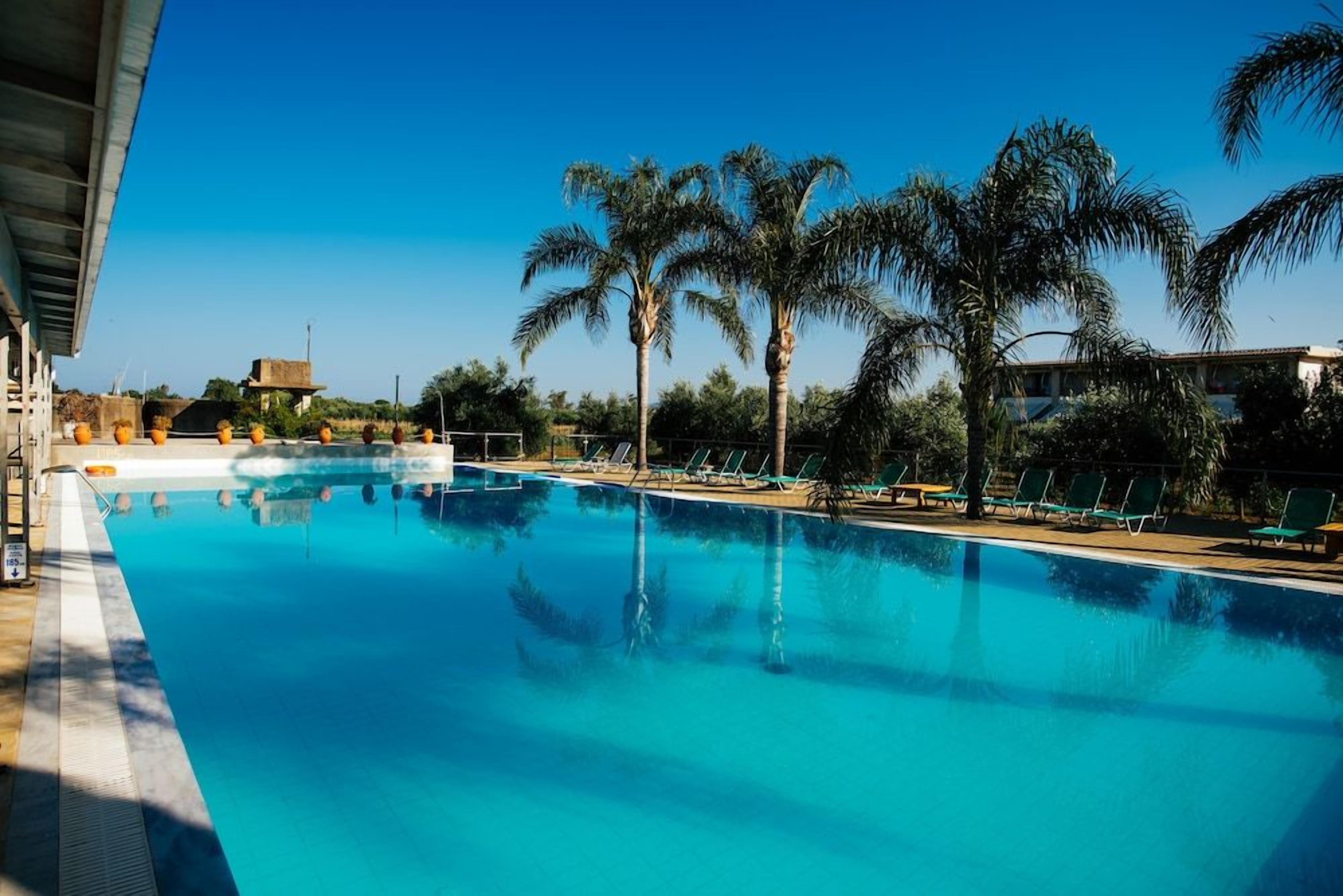 A swimming pool with lounge chairs and palm trees.