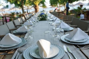 Una larga mesa de comedor dispuesta con platos, vasos y cubiertos, rodeada de sillas.