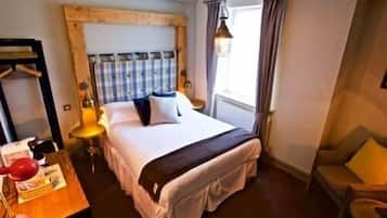 Une chambre d’hôtel avec un lit, une table de chevet, une lampe, une chaise et une fenêtre avec des rideaux.