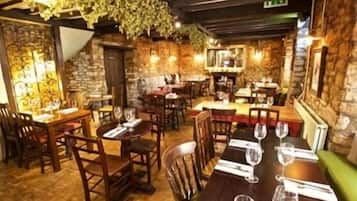 L'intérieur d'un restaurant avec des tables et des chaises en bois, et un mur en pierre en arrière-plan.