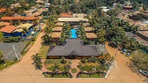 Vista aérea de um resort com vários edifícios, piscina e vegetação exuberante.