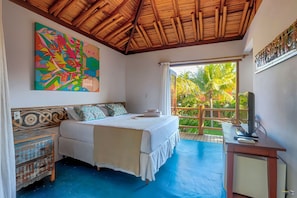 Quarto com cama, escrivaninha, televisão e varanda com vista para palmeiras.