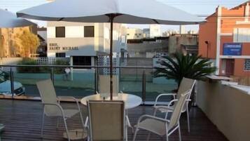 Um deck externo com mesa e cadeiras, um guarda-sol grande e vista para um edifício com letreiros.