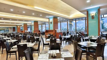 A spacious dining area with multiple tables and chairs, large windows offering a city view, and a modern interior design.