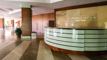 A reception desk with a sign reading '15 Temmuz Gaziler Salonu' in a spacious lobby with a tiled floor and a potted plant.