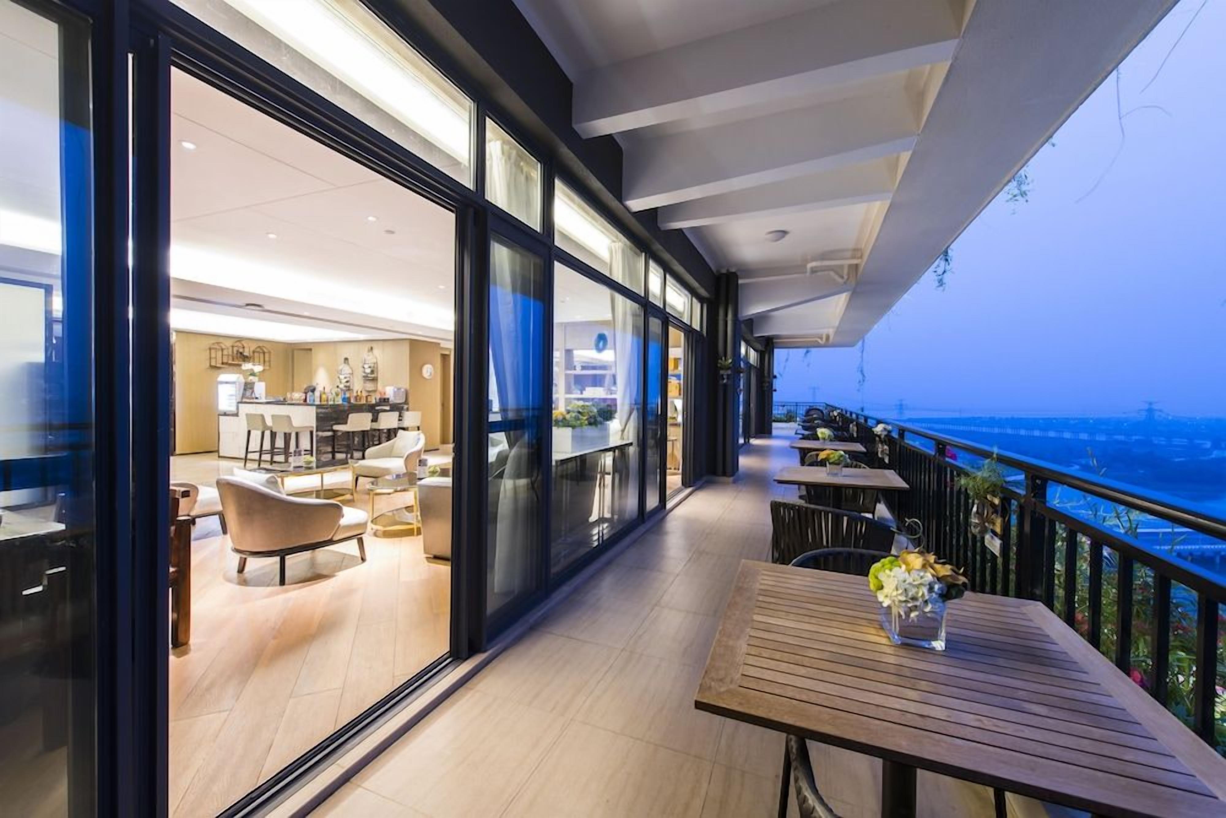 Ein moderner Hotelbalkon mit Meerblick, ausgestattet mit Holztischen und -stühlen, und eine Glaswand, die zu einem Essbereich führt.