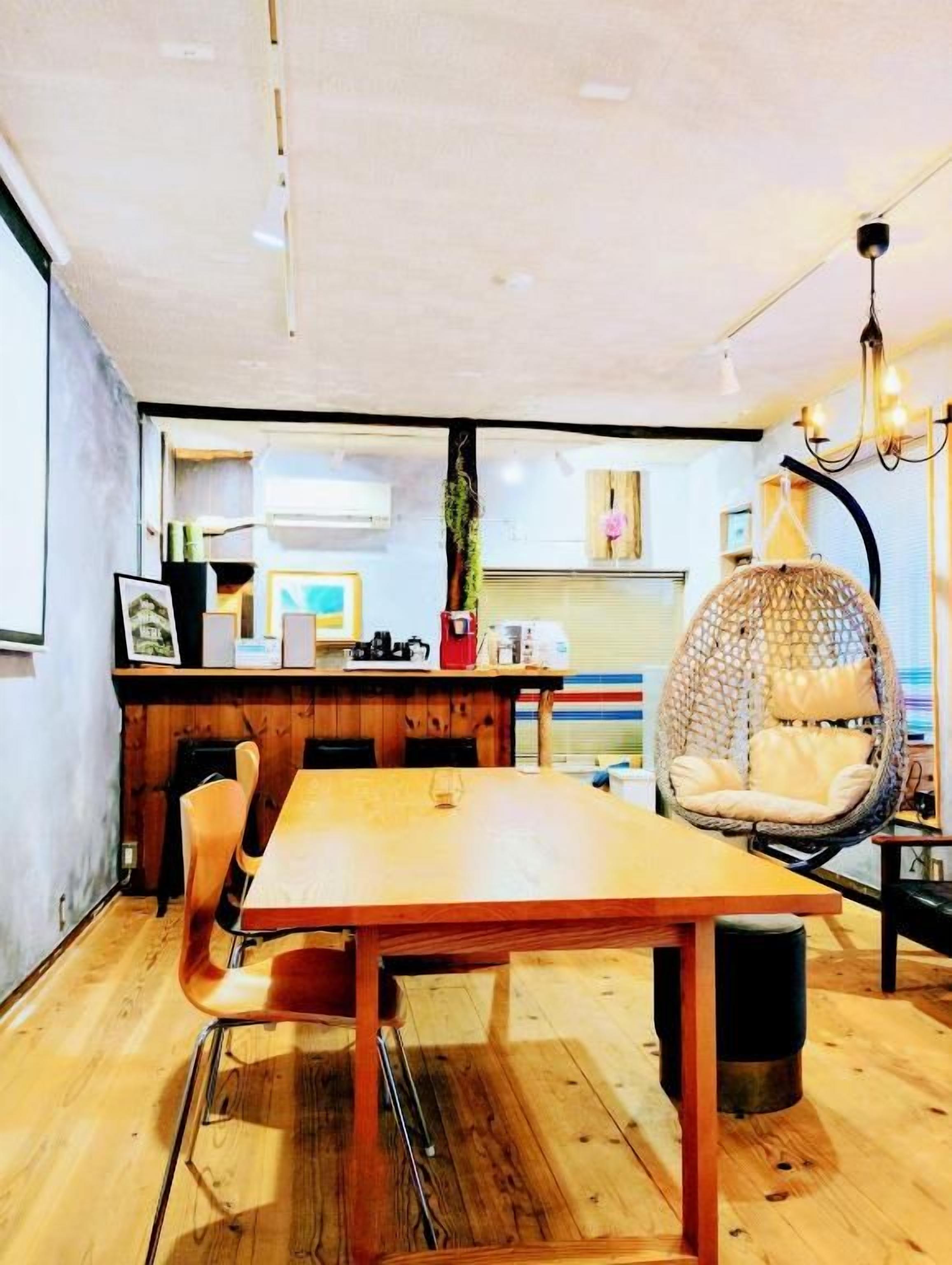A dining area with a wooden table and chairs, a hanging chair, and a kitchen in the background.