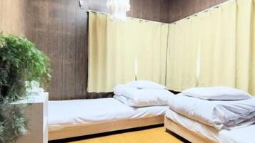 A room with two single beds, a wooden floor, a potted plant, a hanging light fixture, and a ceiling-mounted air conditioning unit.