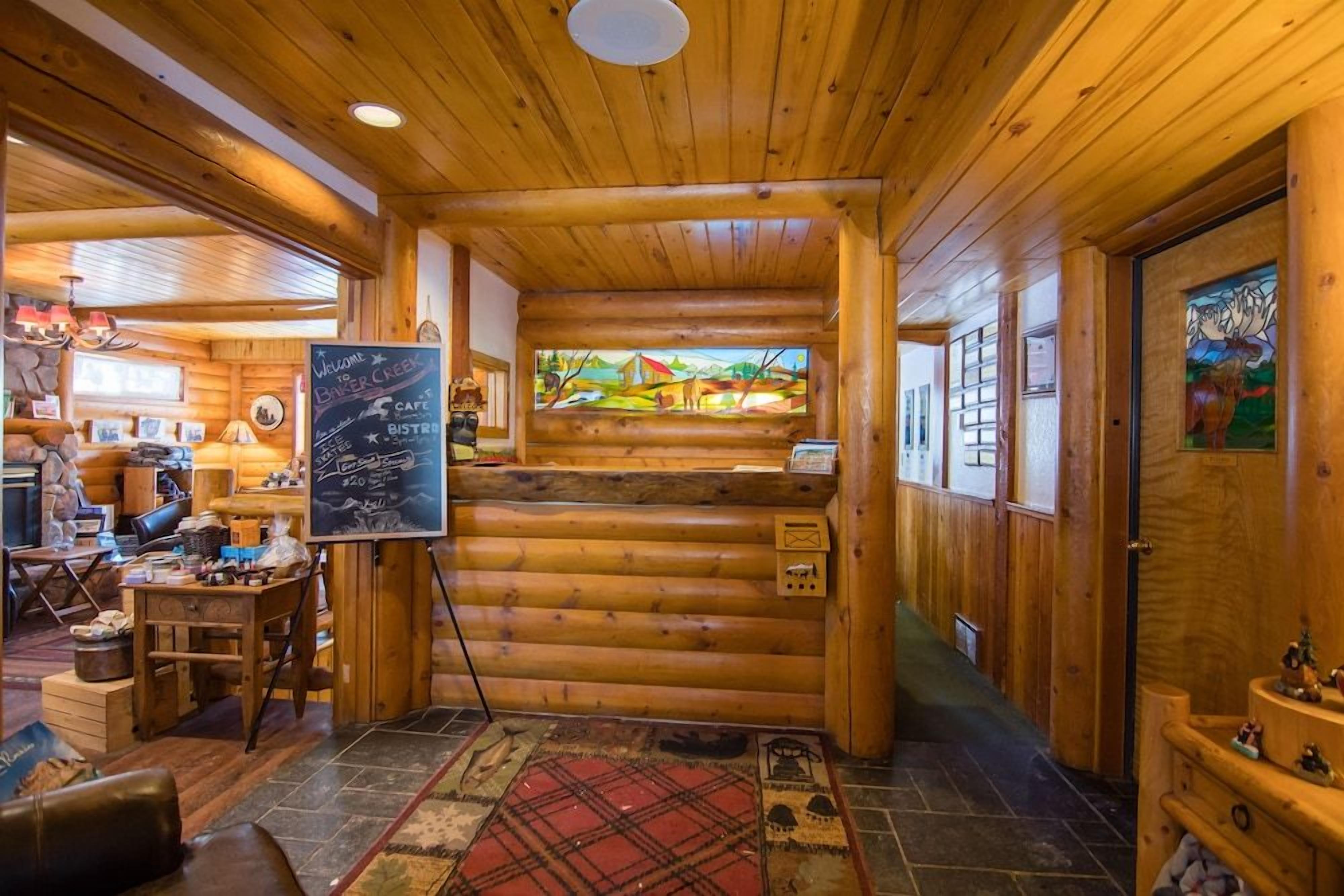 A log cabin interior with a wooden ceiling, a chalkboard menu, a stained glass window, and a fireplace.