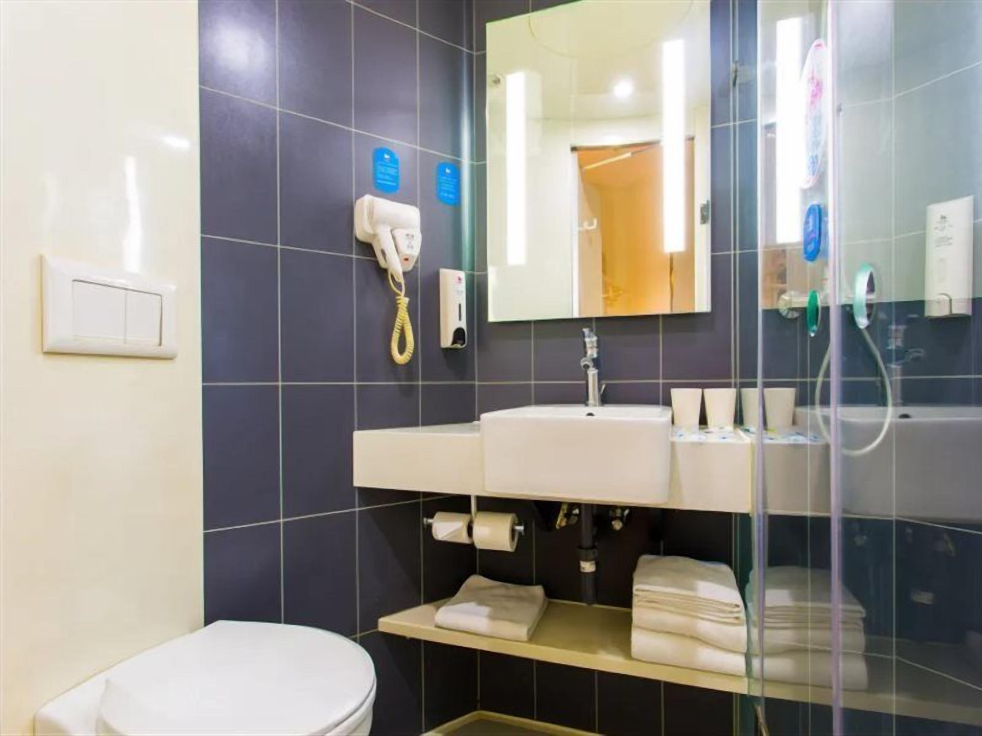 Un baño moderno con inodoro, lavabo y ducha. Hay un espejo sobre el lavabo y un perchero debajo.