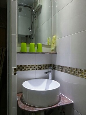 A bathroom with a white sink, a shower, and a mirror. - Sea View Hotel (Kowloon)