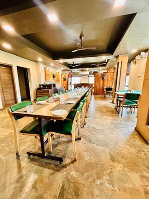 A long dining table with green upholstered chairs in a well-lit room with a ceiling fan. - The Candlewood Park Beach Resort (Kanthi)