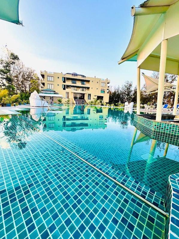 A swimming pool with a tiled floor and a building in the background. - The Candlewood Park Beach Resort (Kanthi)
