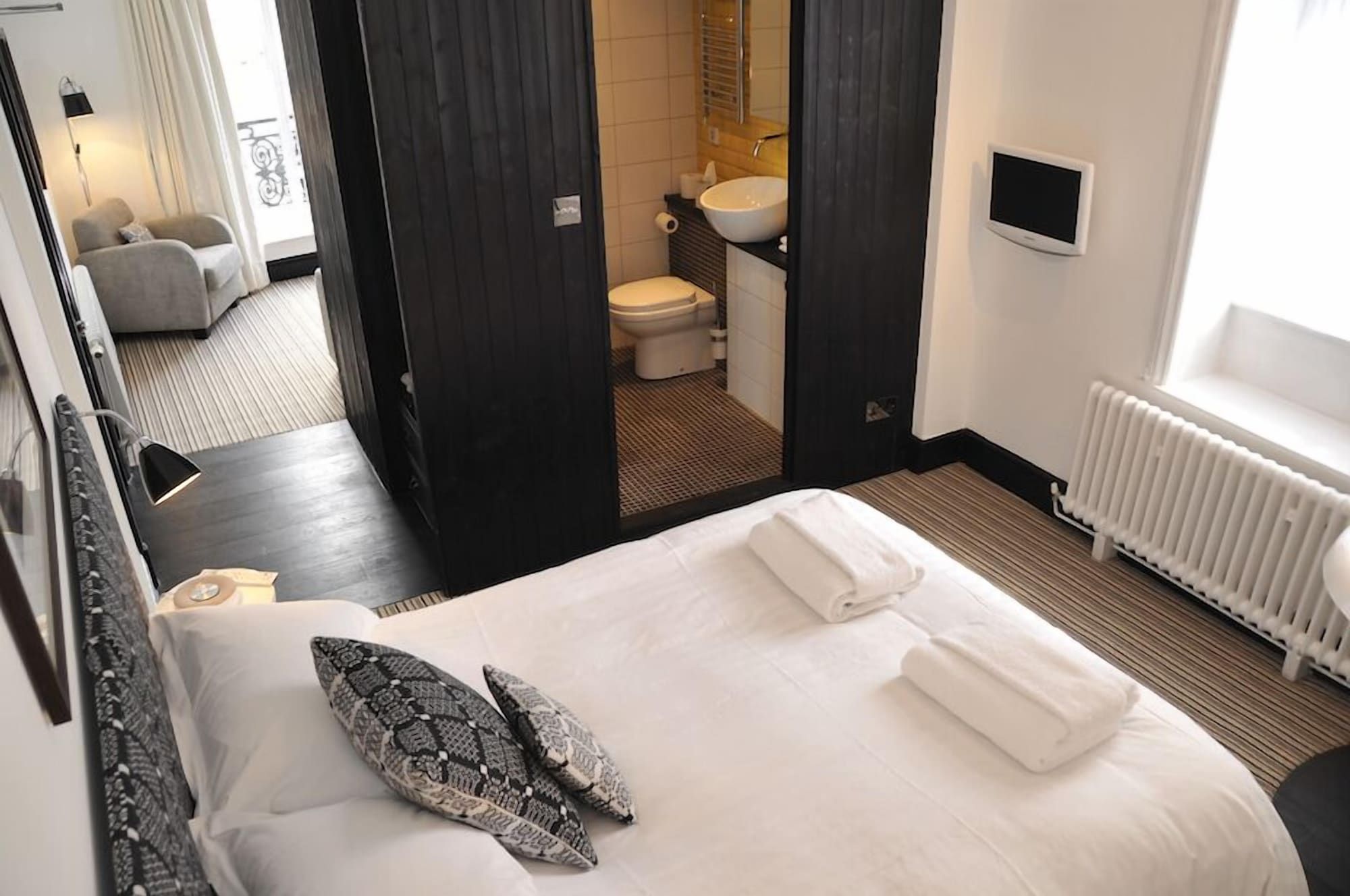 A hotel room with a bed, a bathroom visible through an open door, a radiator, and a TV on the wall.