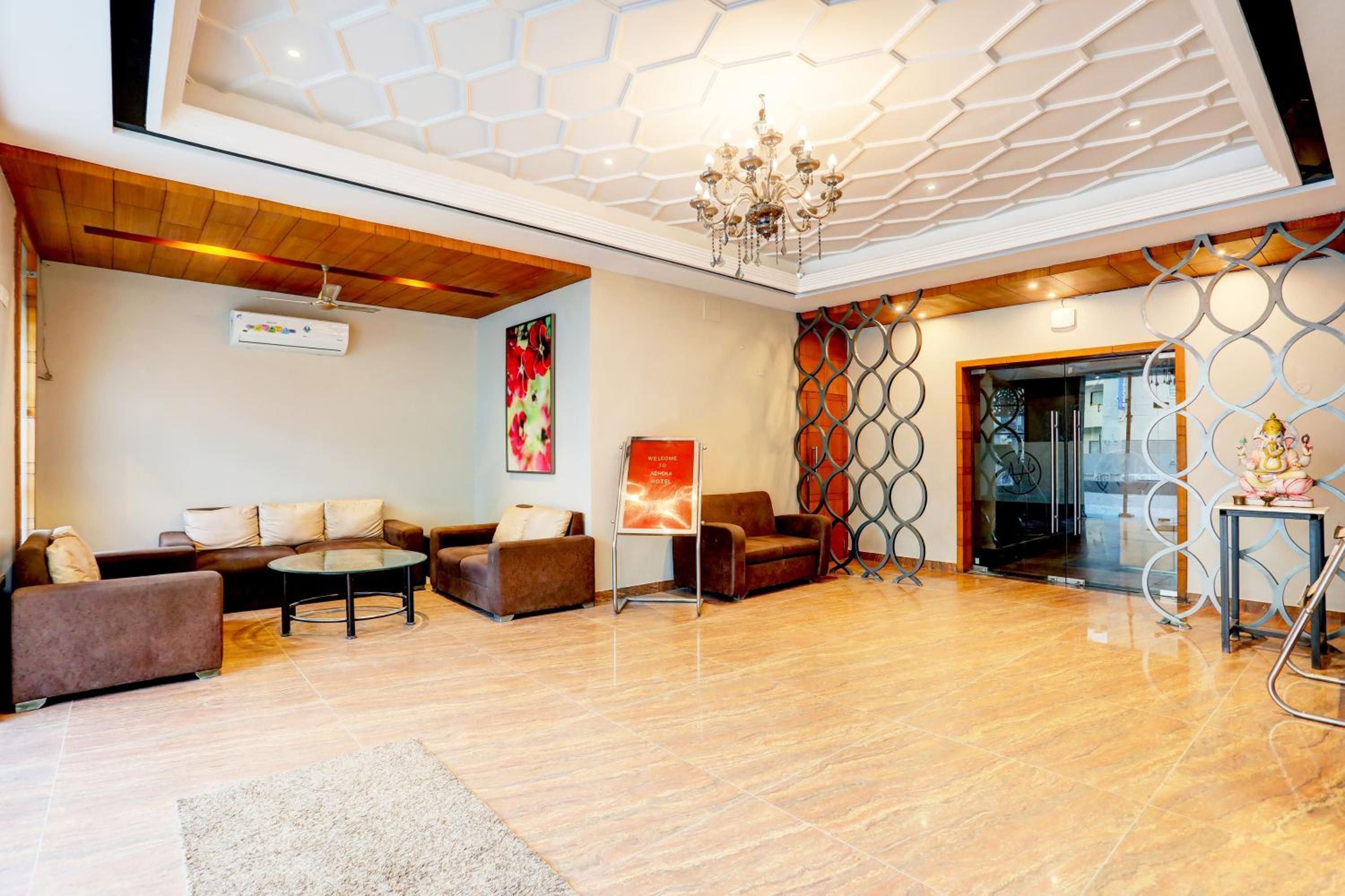 A hotel lobby with a modern chandelier, a reception desk, and a seating area with sofas and a coffee table.