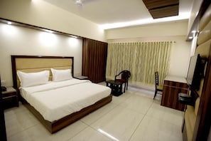 A hotel room with a large bed, a desk, a chair, a television, and a curtain. - Hotel Sach Regency (Anand)