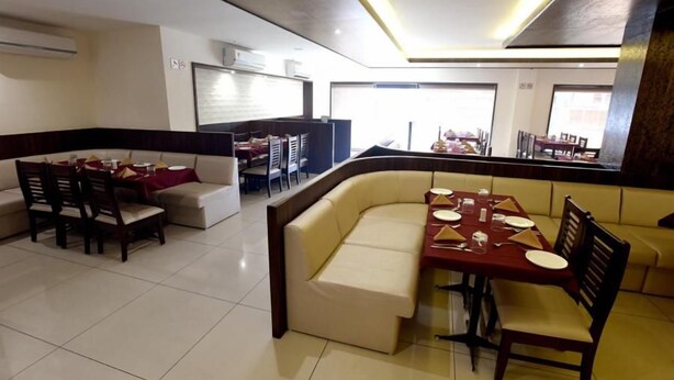 A dining area with a booth seating arrangement and a separate dining table with chairs. - Hotel Sach Regency (Anand)