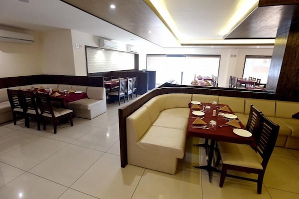 A dining area with a booth seating arrangement and a separate dining table with chairs. - Hotel Sach Regency (Anand)