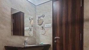 A bathroom with a sink, mirror, towel rings, and a door. - Hotel Sach Regency (Anand)