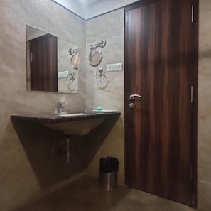 A bathroom with a sink, mirror, towel rings, and a door. - Hotel Sach Regency (Anand)