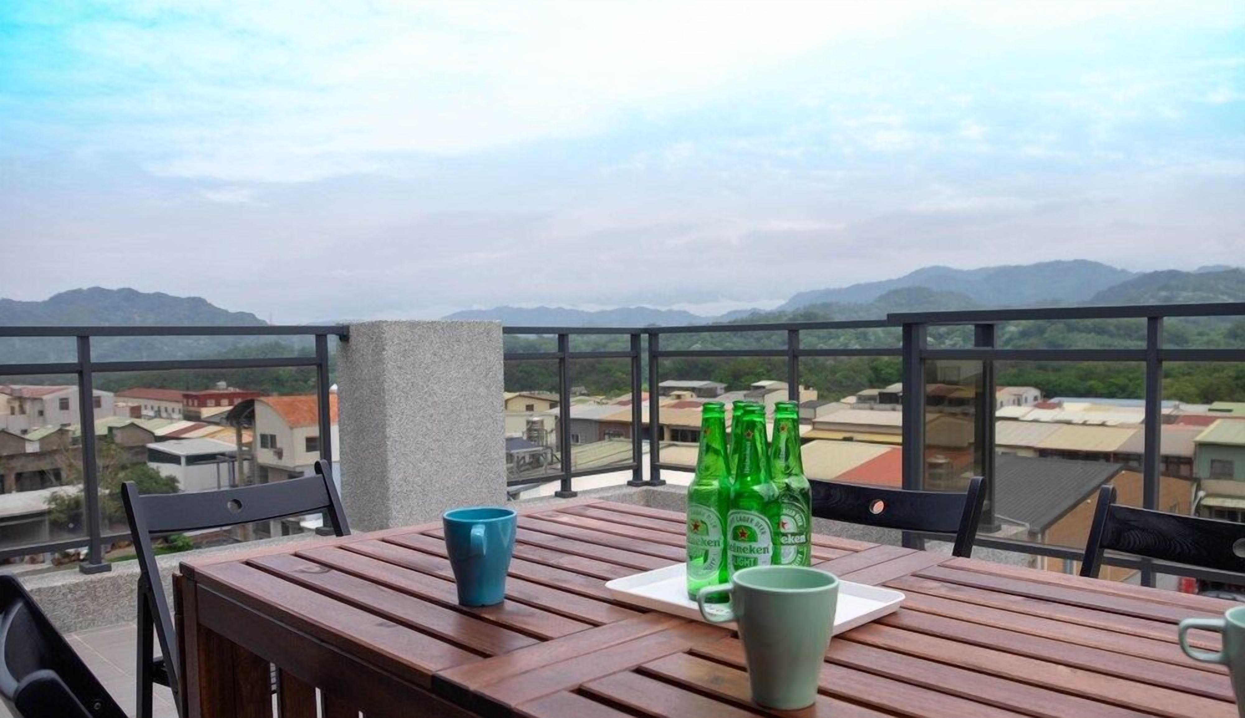 A balcony with a wooden table, two chairs, and a view of distant buildings and mountains.
