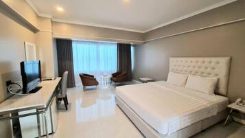 A hotel room with a bed, desk, chairs, and a television.