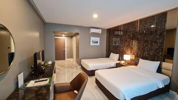 A hotel room with two beds, a desk with a chair, a mirror, and a TV.
