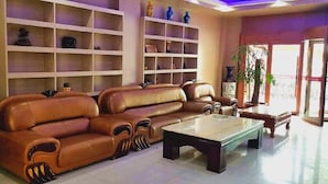 A spacious living area with a brown leather sofa, a coffee table, and shelves with decorative items. - Thank Inn Plus Hotel Shandong Zaozhaung Xuecheng District Wanda Plaza (Zaozhuang)