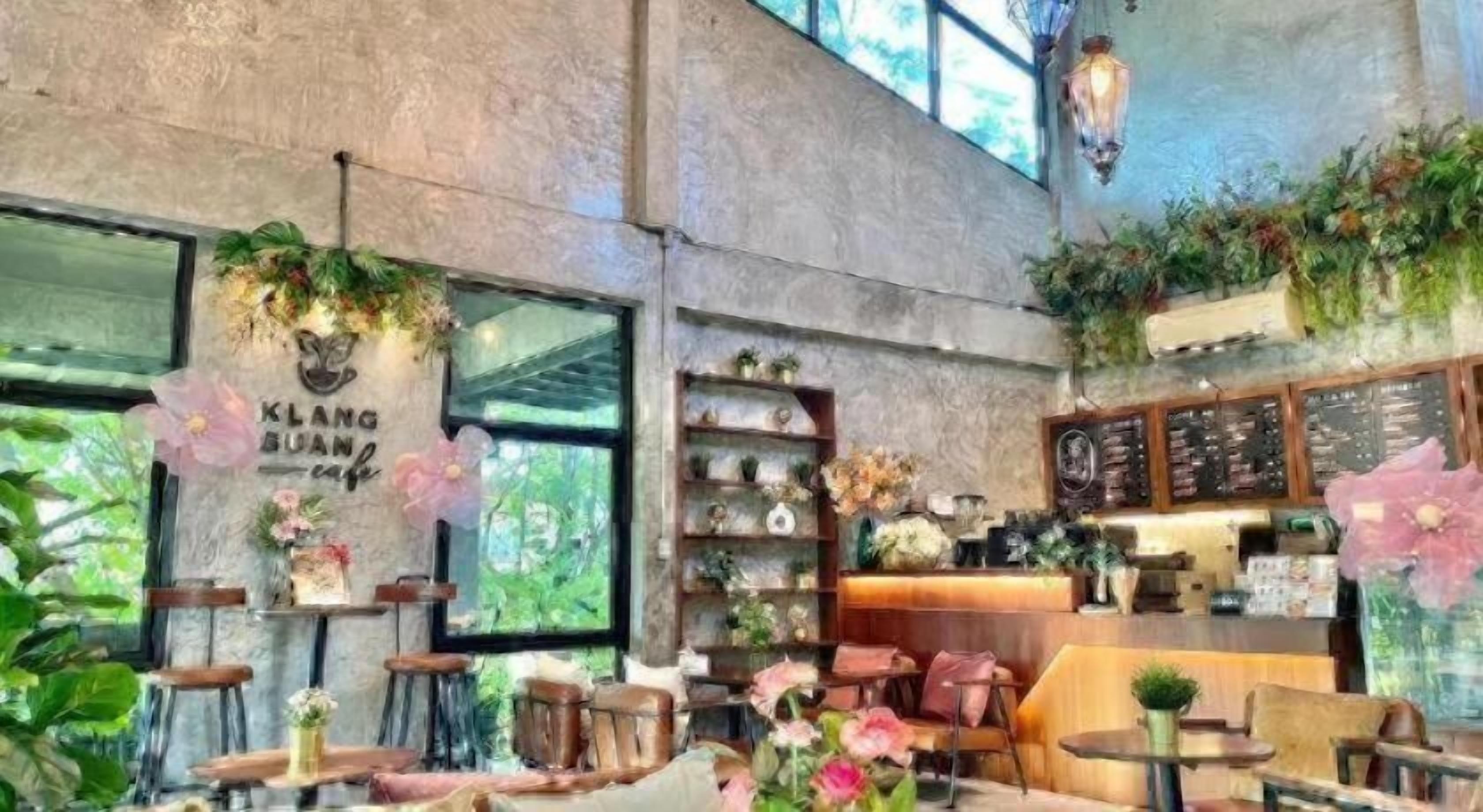 A cafe interior with a high ceiling, wooden tables, chairs, and a counter with a menu board.