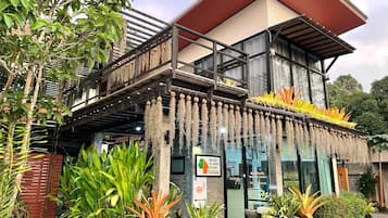 A two-story building with a balcony, surrounded by various plants and greenery.