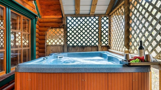 A hot tub with a wooden exterior, surrounded by a wooden fence and a lattice window. - Gnome Alone (Sevierville)