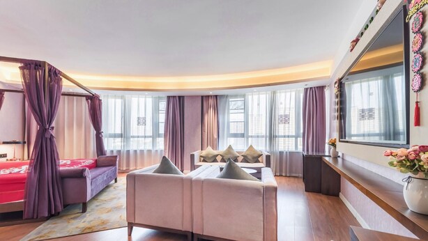 Una habitación de hotel moderna con sofá, cama, zona de comedor y un amplio ventanal con cortinas.