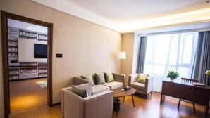Habitación de hotel con sofá, una mesa de centro, escritorio y una ventana grande con cortinas.
