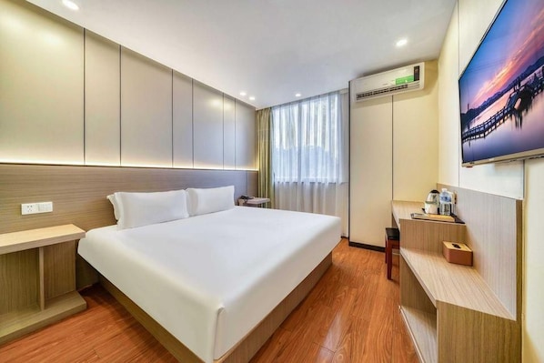 Une chambre d’hôtel avec un grand lit, une table de chevet, un bureau, une chaise, un appareil de climatisation et un téléviseur fixé au mur.