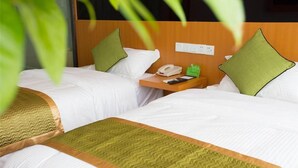 Ein Hotelzimmer mit zwei Betten, jeweils mit weißer Bettwäsche und grünen Kissen. Ein Holznachttisch mit Telefon und einem grünen Beistelltisch sind vorhanden.