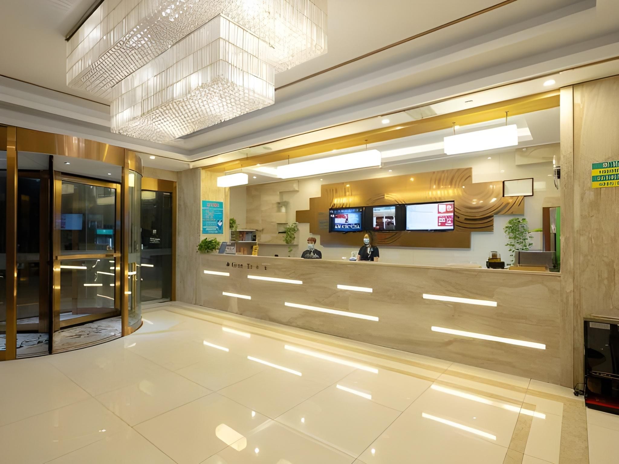 A modern hotel reception area with a marble counter, glass doors, and a large chandelier.