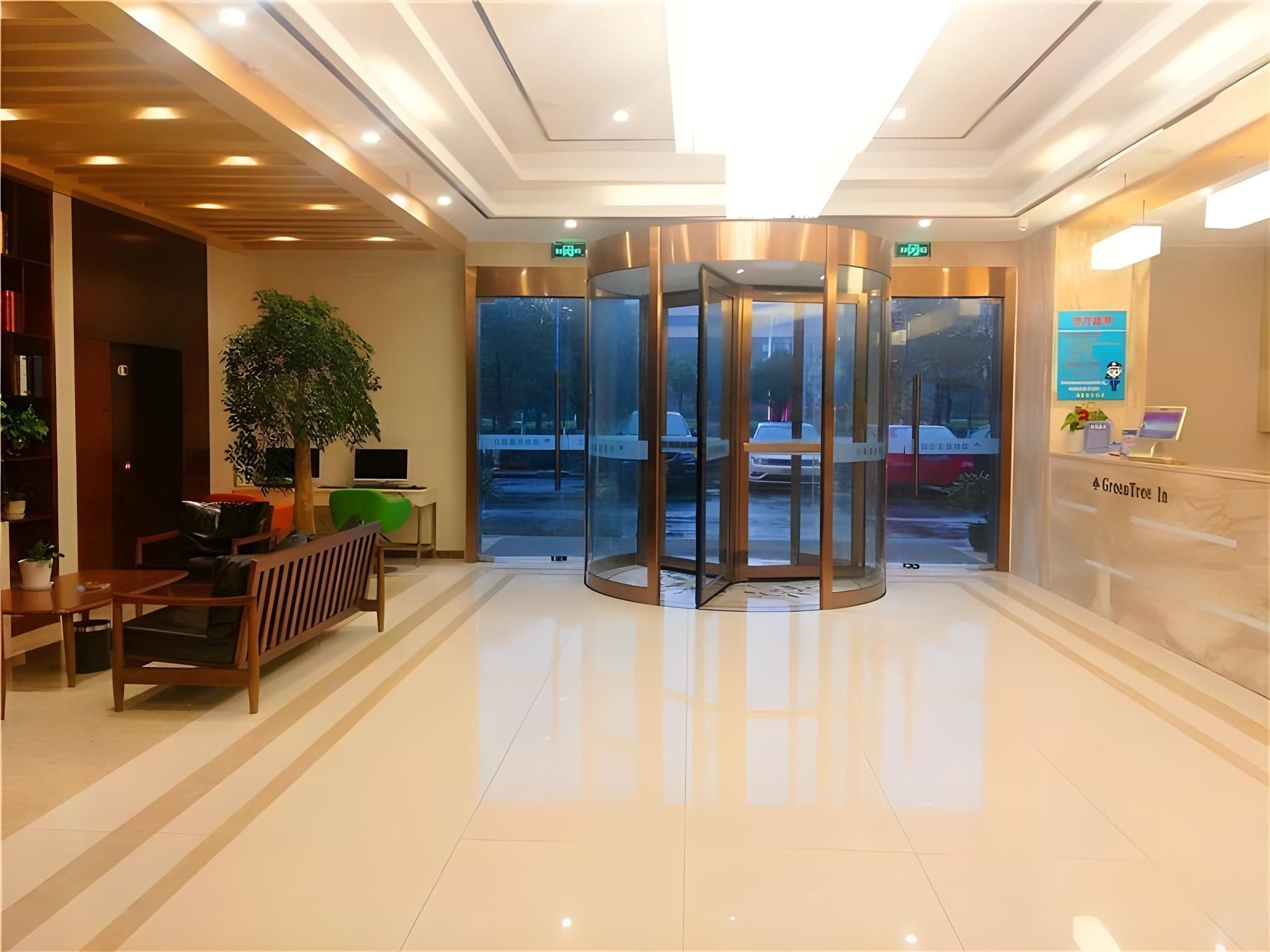A modern lobby with a revolving door, a reception desk, and a seating area with a plant and a laptop.