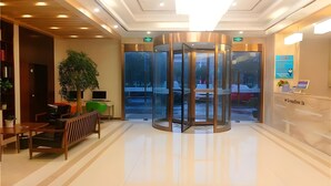 A modern lobby with a revolving door, a reception desk, and a seating area with a plant and a laptop. - Greentree Inn Jiaxing Haiyan Passenger Transport Center Hotel (Jiaxing)