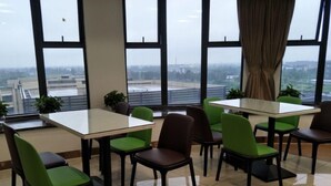 A modern dining area with large windows, green and brown chairs, and a white table. - Greentree Inn Jiaxing Haiyan Passenger Transport Center Hotel (Jiaxing)