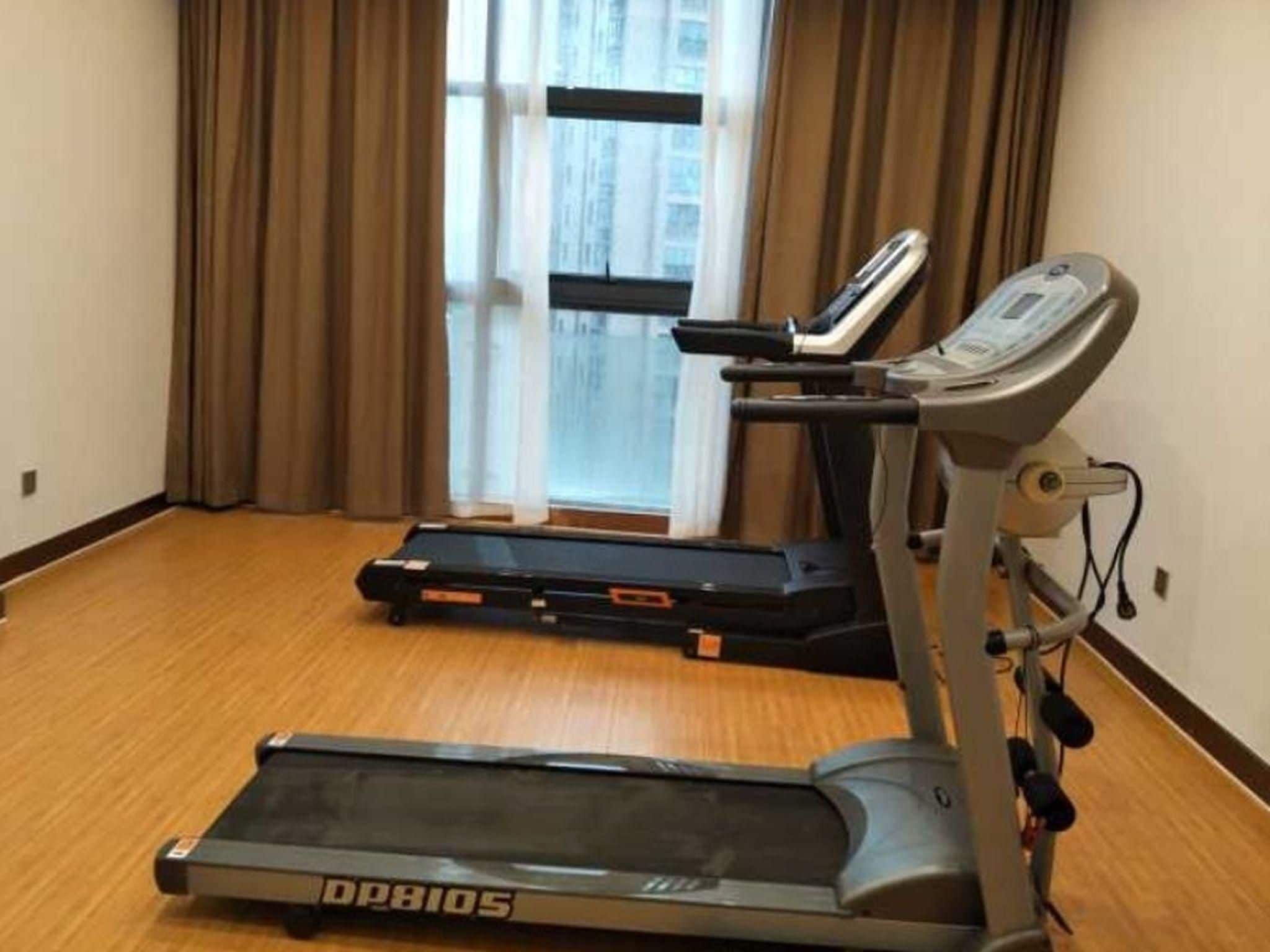 Ein Laufband und ein Indoor-Fahrrad in einem Raum mit Holzboden und einem Fenster mit Vorhängen.