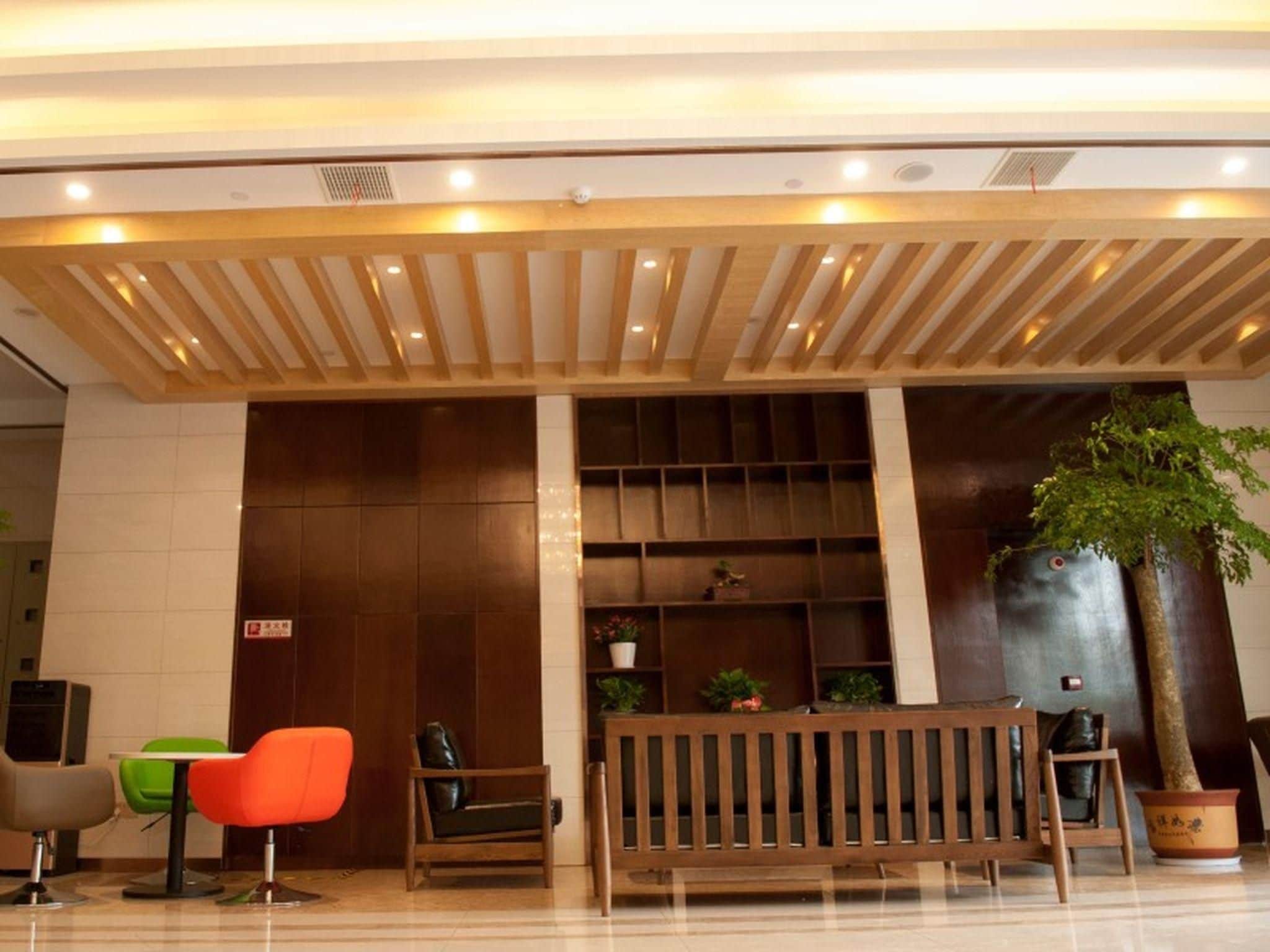 A lobby area with a wooden bench, a green chair, a red chair, and a potted plant.