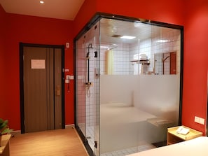 Un baño moderno con separador de vidrio, puerta de madera y una mesita de noche con un teléfono.