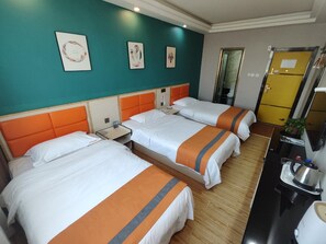 Habitación de hotel con tres camas, una kitchenette pequeña y un baño visible a través de una puerta.