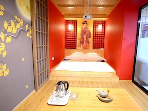 Una habitación con una cama, una mesa con tetera y hervidor, y una obra de arte tradicional japonesa en la pared.