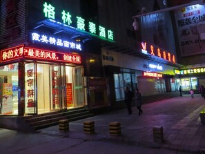 Ein beleuchteter Straßenblick bei Nacht mit leuchtenden Schaufenstern, darunter ein Hotel und ein Geschäft mit einem auffälligen roten Schild.