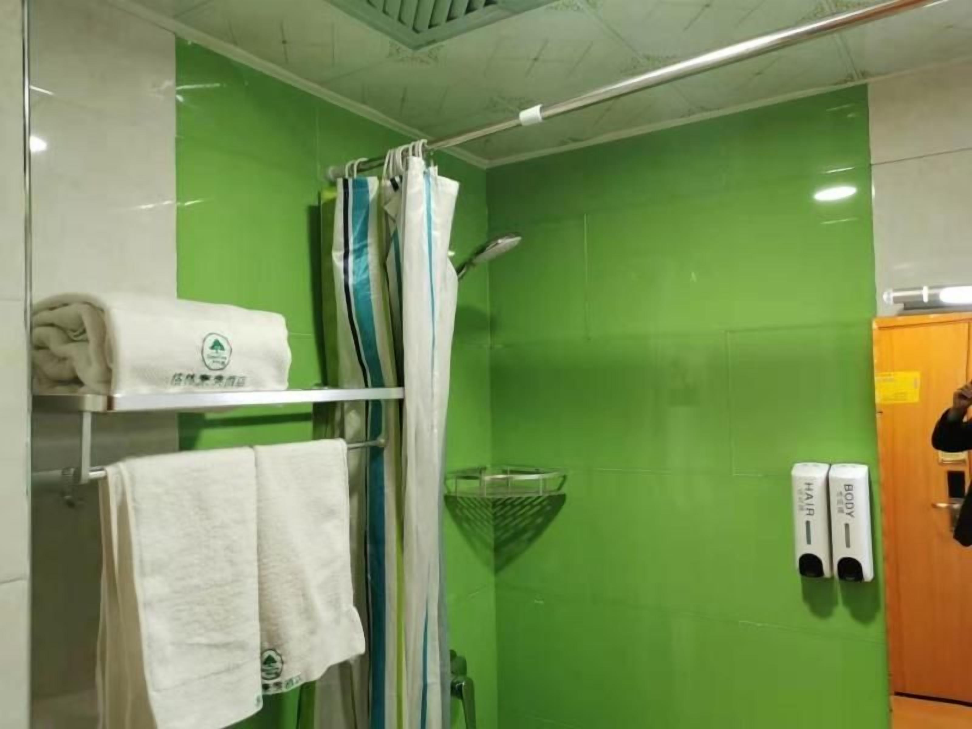Une salle de bain avec un mur vert, une douche avec un rideau et un porte-serviettes avec des serviettes.